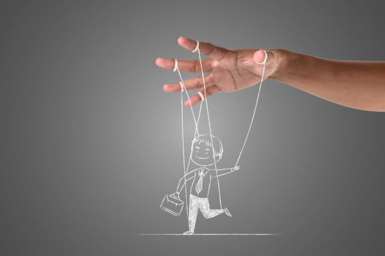 immagine surrealistica della mano di un burattinaio che sorregge con cinque fili il disegno su una lavagna grigia di un uomo d'affari