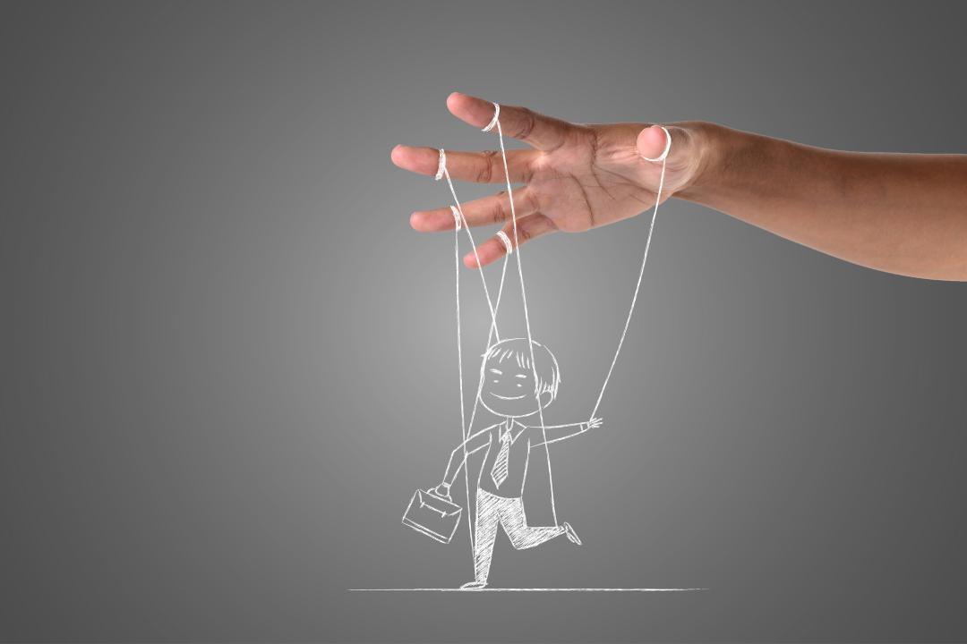 immagine surrealistica della mano di un burattinaio che sorregge con cinque fili il disegno su una lavagna grigia di un uomo d'affari